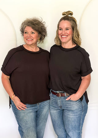 Two women wearing black tops and blue jeans standing against a white background