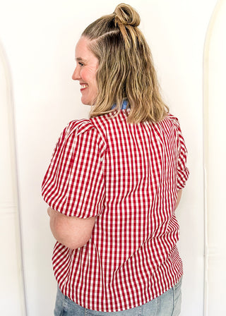 Women’s gingham blouse with decorative buttons and statement neckline detail.