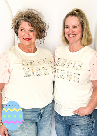 Off white short sleeve shirt with colorful embellished text and pink statement sleeves with decorative pearl studs.