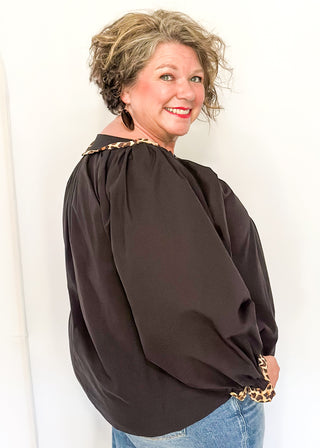 Black long-sleeve blouse with leopard print trim on split neckline and cuffs.