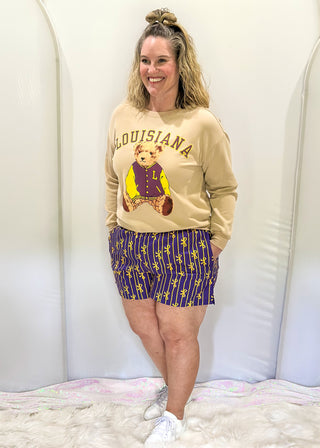 Purple boxer shorts with pockets. Gold stripe pattern with bows throughout. Elastic waist. 