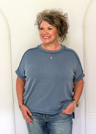 Woman wearing a blue sweater and jeans standing against a white wall