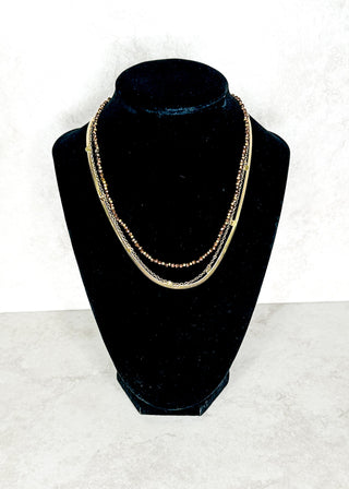 Gold necklace on a black velvet bust against a white background