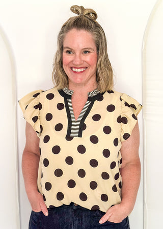 Women's cream blouse with black polka dots, striped split neckline, and flutter sleeves.