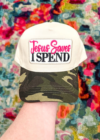 Ivory hat with camo bill and “Jesus Saves I SPEND” embroidered patch in hot pink and black stitching. 