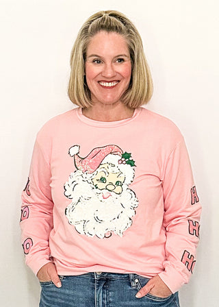 woman modeling a soft pink long sleeve top with sequin Santa face on the front and HO HO HO on the sleeves. 