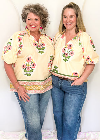 Women's short sleeve ecru top with pink floral bundles and decorative hem and collar. 