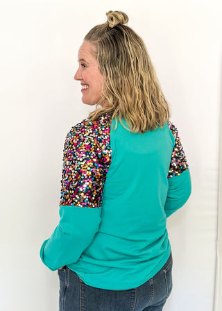 Turquoise long sleeve top with multi color sequin sleeves and chenille ‘MERRY’ lettering across the front.