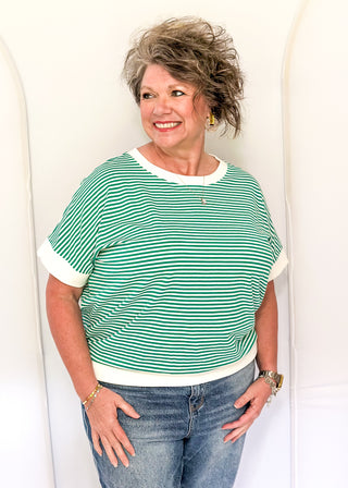 Woman wearing a green and white striped shirt and blue jeans against a white background