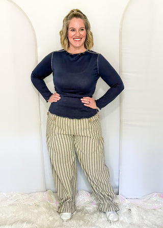 A woman modeling a dark navy long-sleeve top and beige pinstriped pants, standing against a white arched backdrop.
