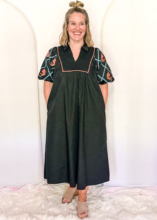 Women wearing a black midi dress with embroidered puff sleeves and a smocked bodice
