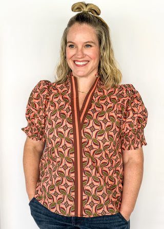 Bubble sleeve V-neck short sleeve top with terracotta, brown and green print. Ribbon detail down the front in brown and terracotta. 