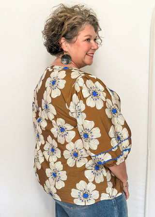 Mocha colored floral blouse featuring white and blue blooms with blue scalloped trim. 