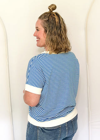 Woman wearing a blue and white striped shirt with rolled-up sleeves, standing against a white background.