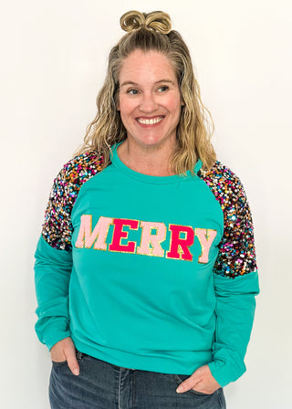 Turquoise long sleeve top with multi color sequin sleeves and chenille ‘MERRY’ lettering across the front.
