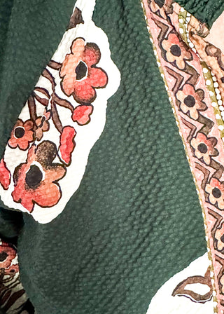 Close up of forest green boho print top featuring smocked collar large floral bundles and colorful border trim.