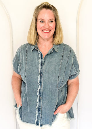 Denim button-down top with short sleeves, pointed collar, vertical stitched panels, and frayed raw-edge hem.