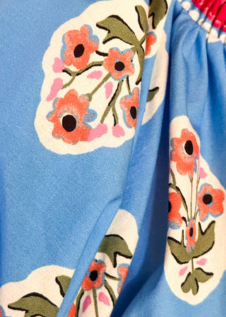 close up of bright blue 3/4 sleeve top with floral pattern, smocked collar with matching coral floral neckline and hem. 