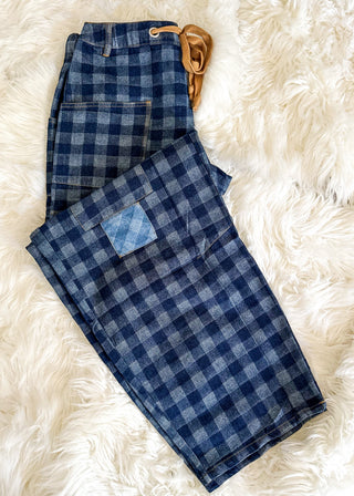 A pair of folded blue and gray plaid flannel pants with a tan leather belt, laid flat on a white faux fur background.