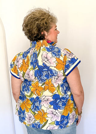 Floral top featuring blue, yellow, and lavender blooms with blue contrast trim on neckline and sleeves.
