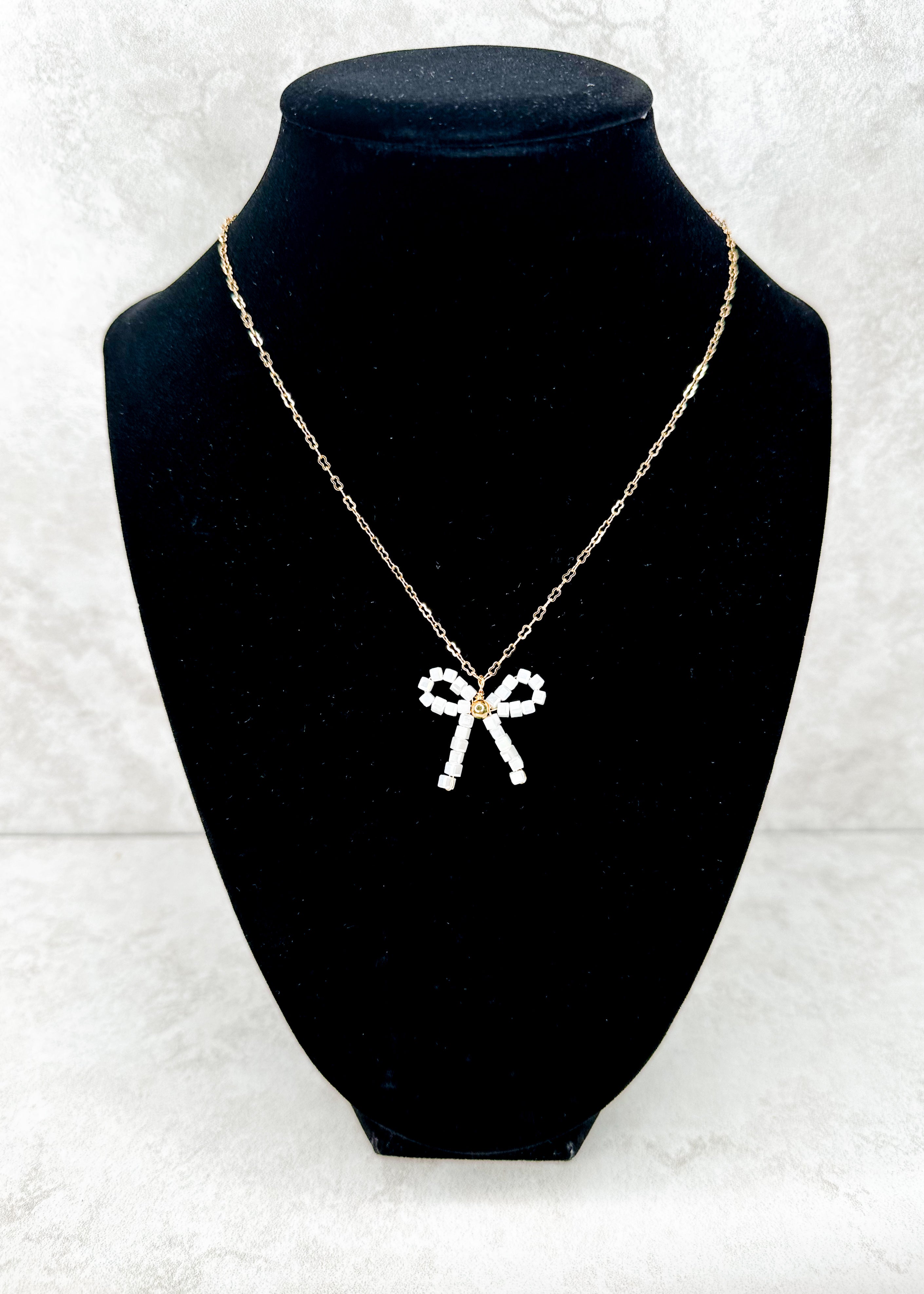 gold chain necklace with white beaded bow pendant