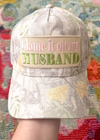 Light camouflage snap back cap with “Blame It On My Husband” embroidered patch