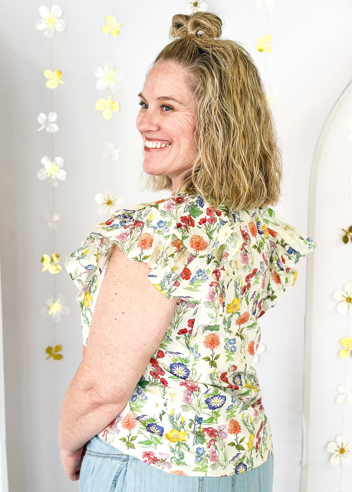 Multi-color wildflower print short sleeve top with ruffle sleeve and tie detail at the neck. 