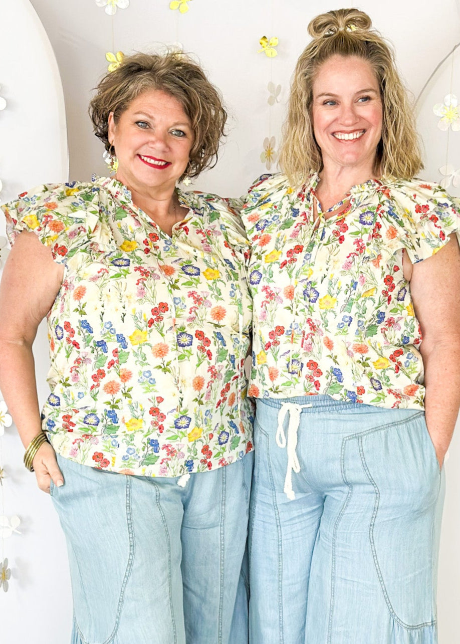 Multi-color wildflower print short sleeve top with ruffle sleeve and tie detail at the neck. 