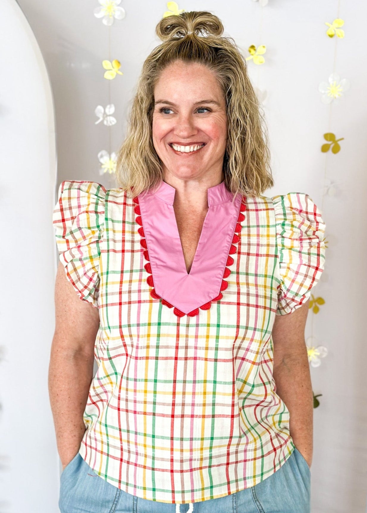 Ivory ruffle sleeve top with red, pink, yellow, and green plaid stripes.  V-neck with solid pink and red scallop detail around the collar and surrounding the v-neck. 