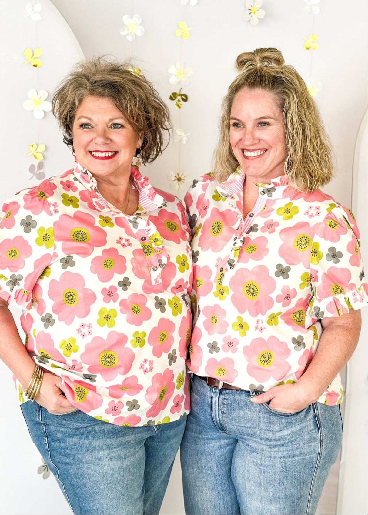 lightweight short sleeve blouse. Ruffle detail around the collar, sleeves and down the front highlighting the 4 button closure.  White background with distressed flowers in pink, lime and dark gray.