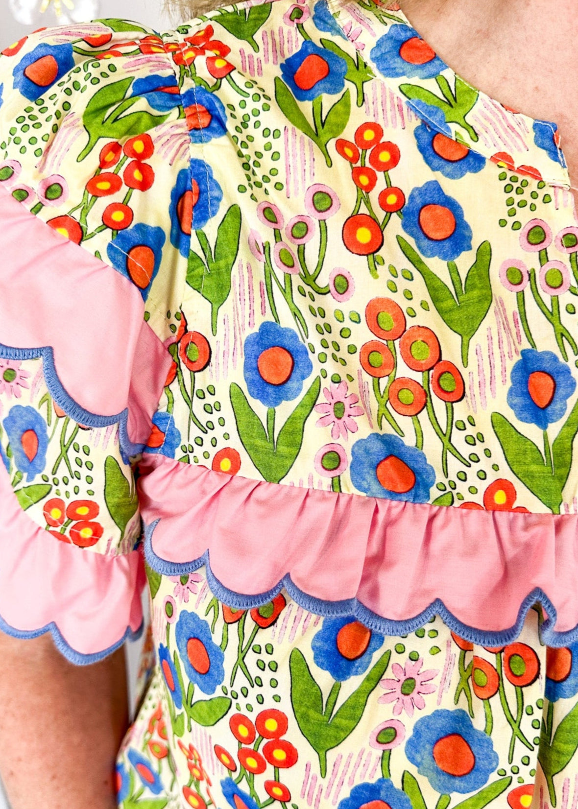 lightweight short sleeve v-neck blouse. Small pink, blue and orange flowers with pink scallop ruffle detail on the sleeve and across the chest. 