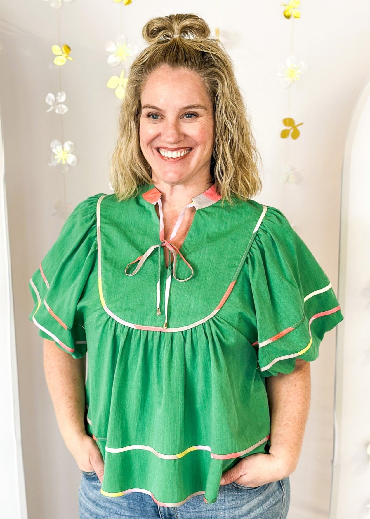 Green babydoll v-neck top with oversized balloon sleeve. multicolored piping detail on sleeve, hem, and collar.  Matching tie closure off of the collar. 