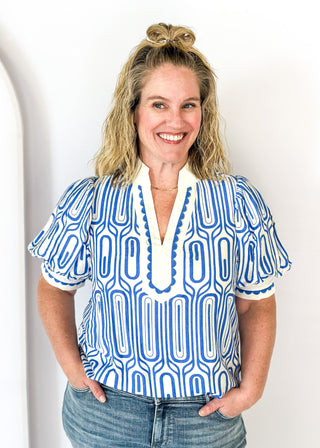 blue geometric pattern on off white puff short sleeve top - off white banding detail around collar and v-neck - blue scallop trim detail around v-neck and on cream banding around cuff