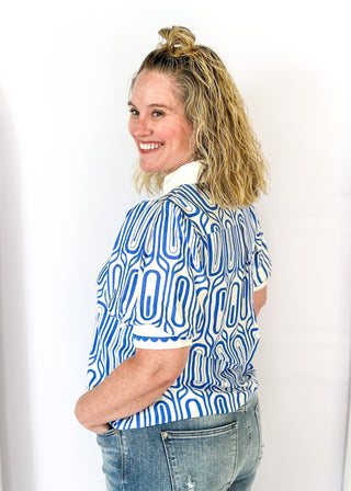 blue geometric pattern on off white puff short sleeve top - off white banding detail around collar and v-neck - blue scallop trim detail around v-neck and on cream banding around cuff
