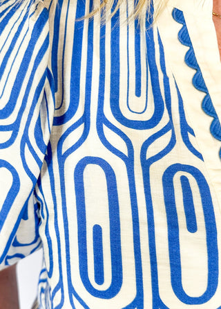 blue geometric pattern on off white puff short sleeve top - off white banding detail around collar and v-neck - blue scallop trim detail around v-neck and on cream banding around cuff