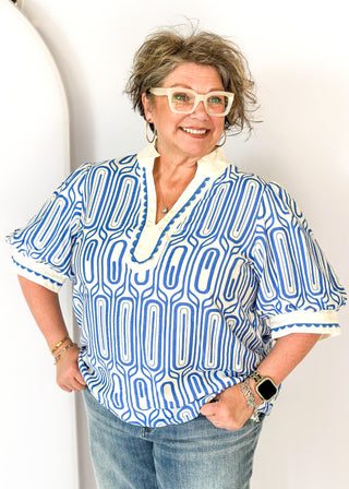 blue geometric pattern on off white puff short sleeve top - off white banding detail around collar and v-neck - blue scallop trim detail around v-neck and on cream banding around cuff