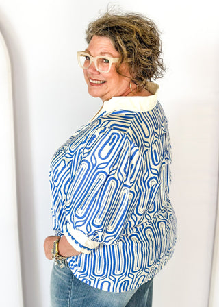 blue geometric pattern on off white puff short sleeve top - off white banding detail around collar and v-neck - blue scallop trim detail around v-neck and on cream banding around cuff