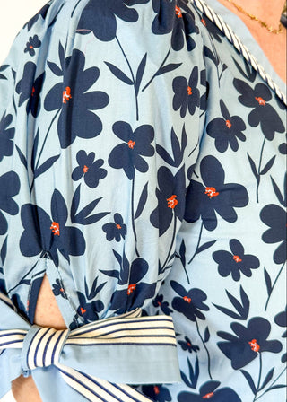 light blue top with navy flowers and red centers - light blue band around v-neck and straight down the front with blue and white striped trim along side it - light blue and striped bow at cuff