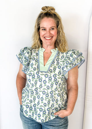 Mint and blue flowers with green stems on a cream background double ruffle short sleeve top - v-neck - mint band around ruffle collar and v-neck - blue and white piping detail around double ruffle short sleeves and v-neck