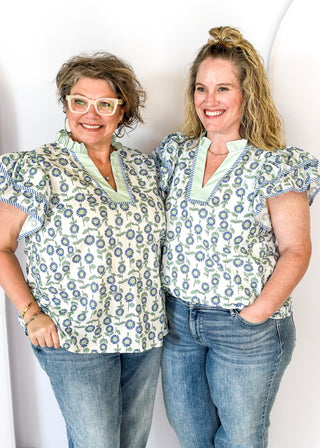 Mint and blue flowers with green stems on a cream background double ruffle short sleeve top - v-neck - mint band around ruffle collar and v-neck - blue and white piping detail around double ruffle short sleeves and v-neck