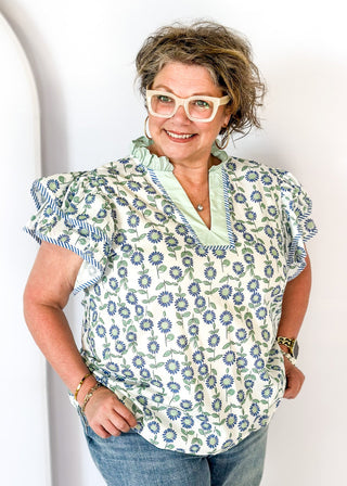 Mint and blue flowers with green stems on a cream background double ruffle short sleeve top - v-neck - mint band around ruffle collar and v-neck - blue and white piping detail around double ruffle short sleeves and v-neck