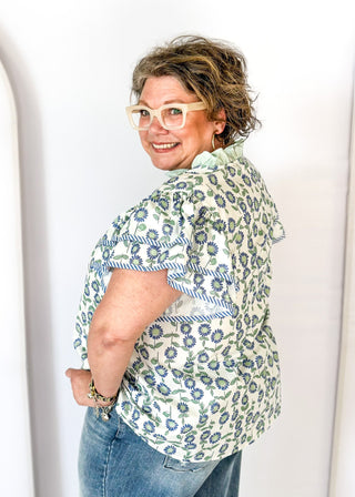 Mint and blue flowers with green stems on a cream background double ruffle short sleeve top - v-neck - mint band around ruffle collar and v-neck - blue and white piping detail around double ruffle short sleeves and v-neck