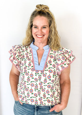 red and blue flowers with green stems on a cream background double ruffle short sleeve top - v-neck - light blue band around ruffle collar and v-neck - candy strip red and white piping detail around double ruffle short sleeves and v-neck