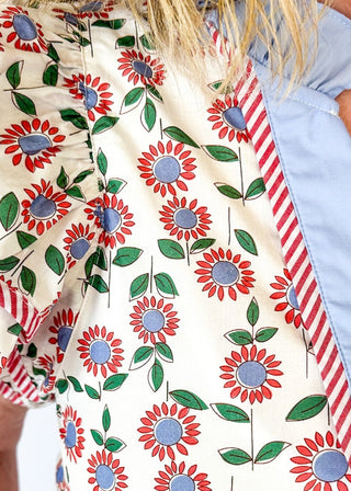 red and blue flowers with green stems on a cream background double ruffle short sleeve top - v-neck - light blue band around ruffle collar and v-neck - candy strip red and white piping detail around double ruffle short sleeves and v-neck