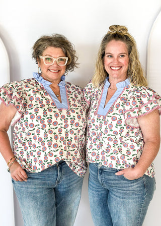 red and blue flowers with green stems on a cream background double ruffle short sleeve top - v-neck - light blue band around ruffle collar and v-neck - candy strip red and white piping detail around double ruffle short sleeves and v-neck