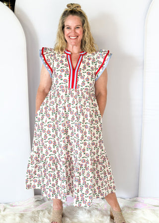 white maxi dress with red and blue flowers and green stems/leaves - tiered - red and blue ribbon trim around v-neckline - and red and blue trim around double ruffle sleeve - pockets