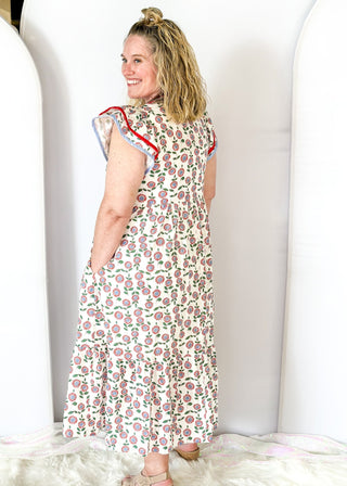 white maxi dress with red and blue flowers and green stems/leaves - tiered - red and blue ribbon trim around v-neckline - and red and blue trim around double ruffle sleeve - pockets