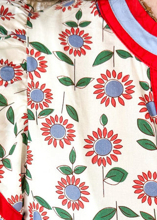 white maxi dress with red and blue flowers and green stems/leaves - tiered - red and blue ribbon trim around v-neckline - and red and blue trim around double ruffle sleeve - pockets