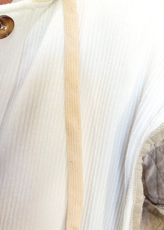 Close-up of a white ribbed knit garment with a beige drawstring and a brown button, showing the fabric texture and details.