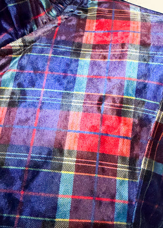 A close-up of a plush velvet fabric with a colorful tartan plaid pattern featuring blue, red, purple, and yellow stripes.